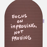 Close-up on the pink quote “focus on improving not proving” on the Hercule Studio x Thomas Lélu sport mat, artistic message and graphic typography